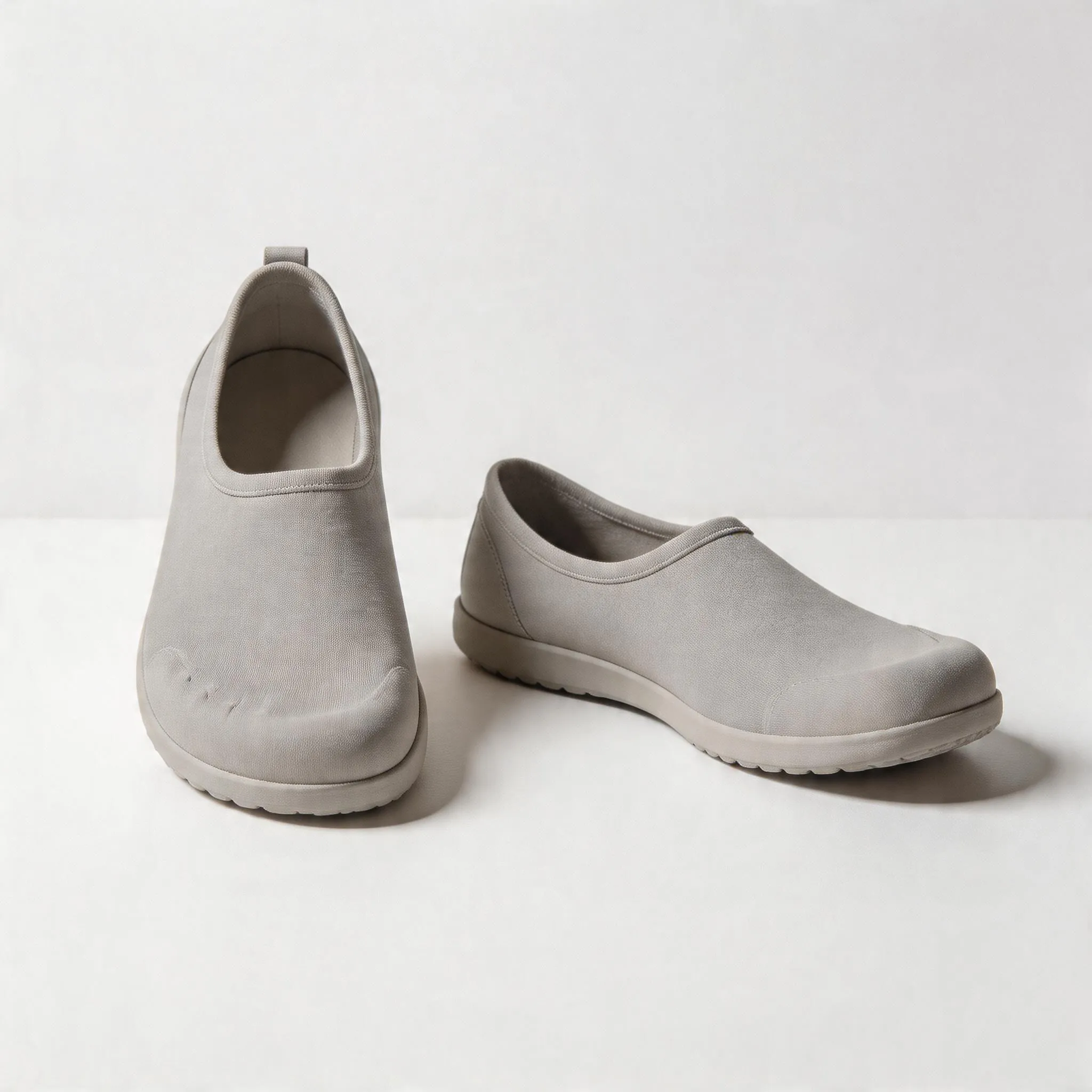 Fotografia di prodotto iperrealistica, scarpe a piedi nudi personalizzabili con suole a caduta zero esposte su una superficie pulita e minimalista, illuminazione professionale in studio, messa a fuoco dei dettagli della scarpa che mostrano l'ampio alloggiamento della punta e la suola flessibile, nessun testo, nessun logo del marchio